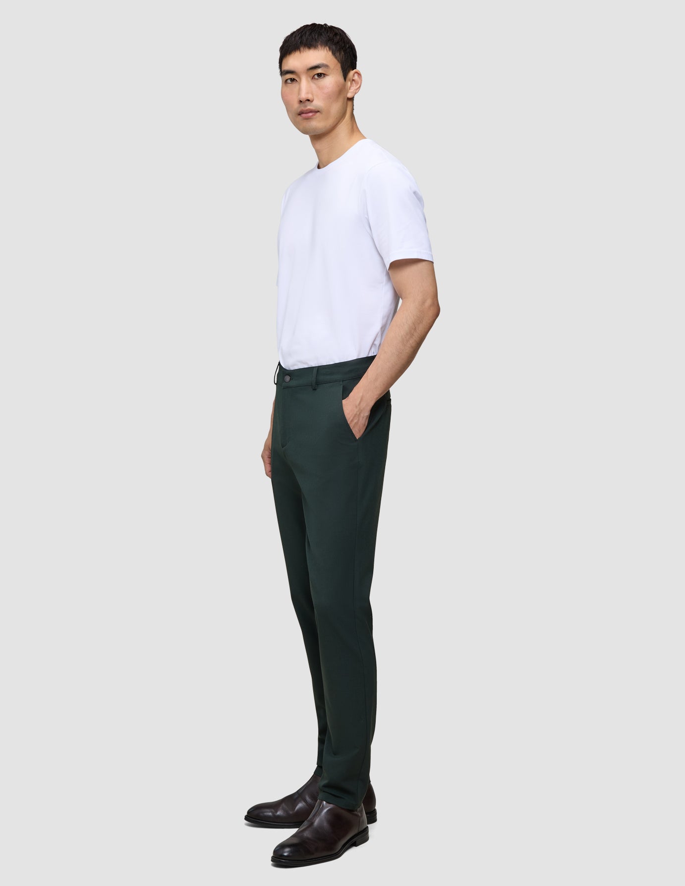En mand i en hvid T-shirt og Ease Pants Regular Northern Pine står set i profil og fremviser klassisk dansk design.